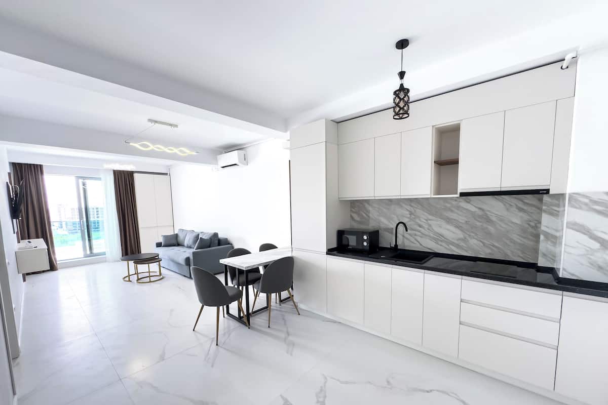 Una cocina moderna con armarios blancos, salpicadero de mármol y un comedor con mesa y sillas.