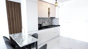 Cozinha moderna com armários brancos, bancada de mármore e torneira preta. Há um espaço de jantar com mesa de mármore e duas cadeiras cinzas.