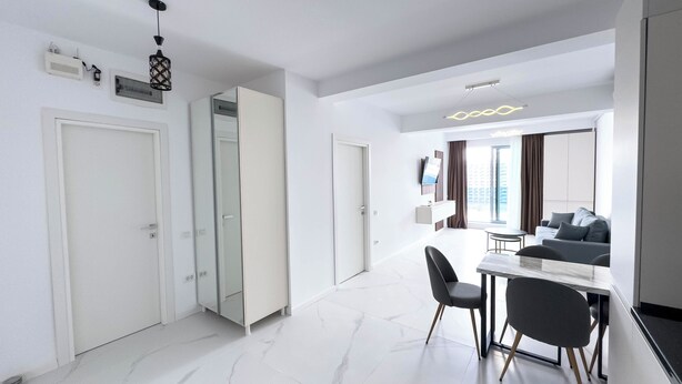 Quarto moderno e bem iluminado, com área de jantar, sofá e televisão.