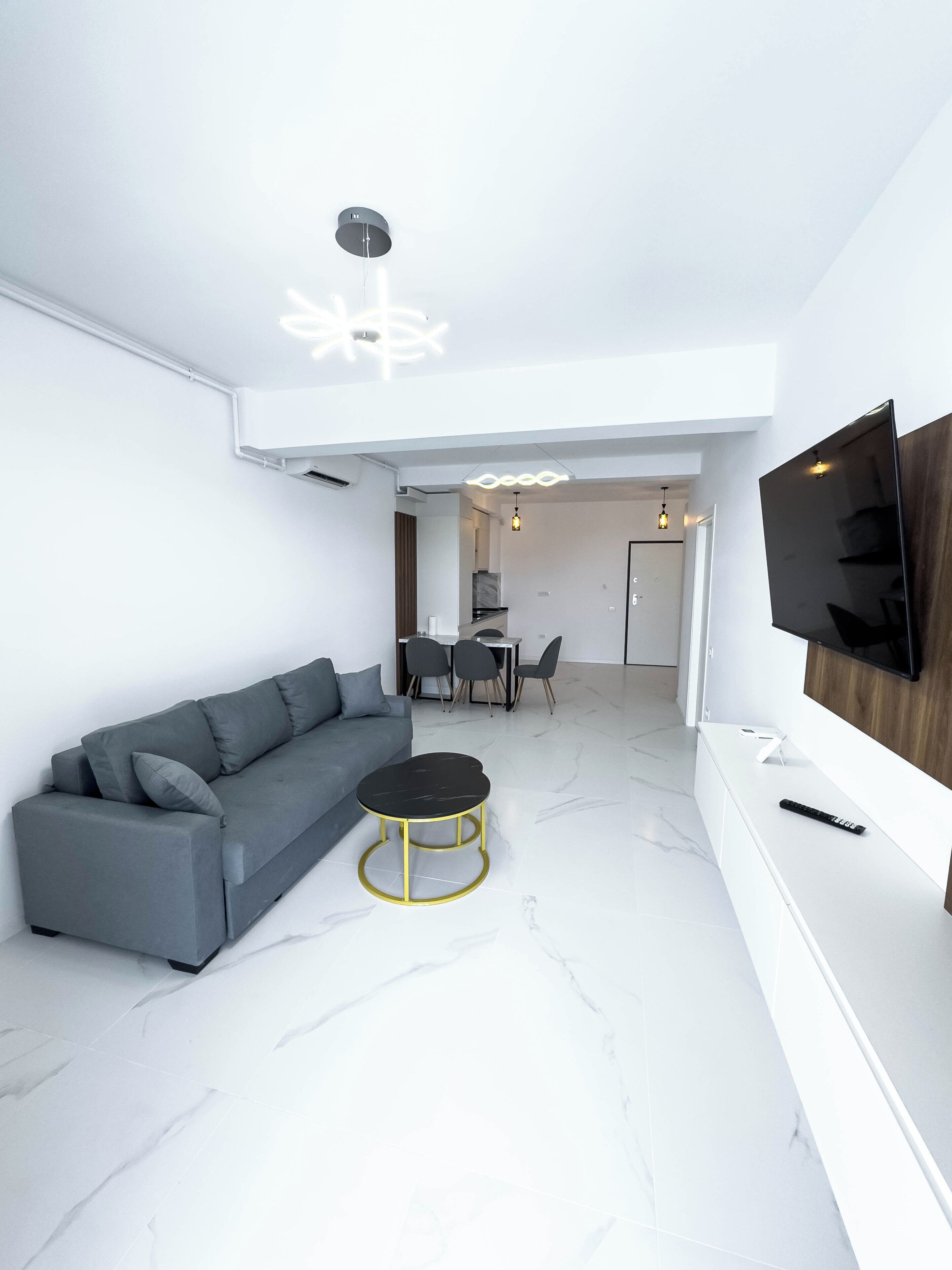 A modern living room with a grey sofa, a round coffee table, and a flat-screen TV mounted on the wall.