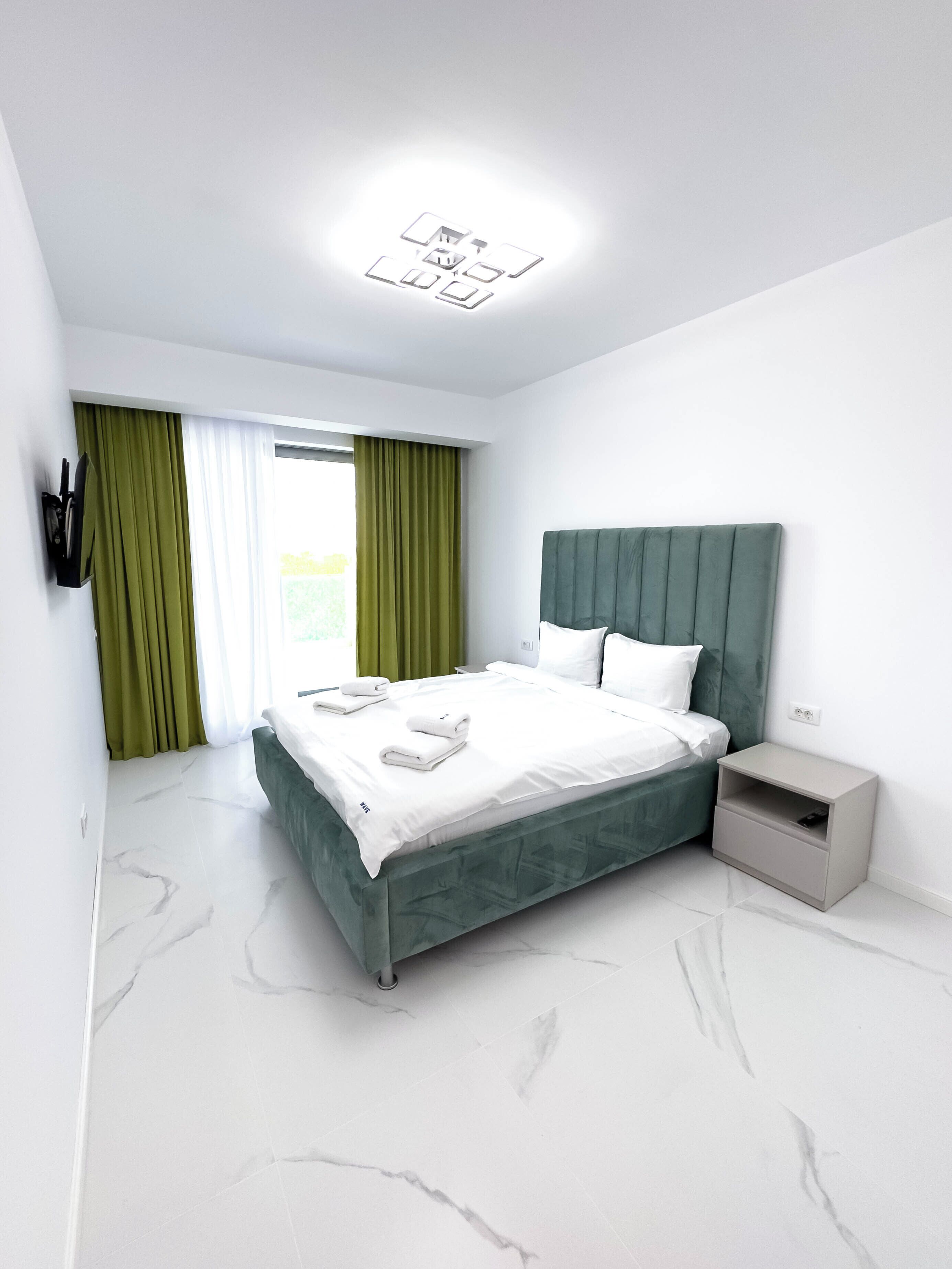 Une chambre moderne avec un grand lit, des rideaux verts, une table de chevet et une commode.