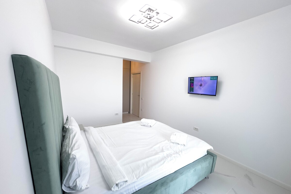 A modern hotel room with a neatly made bed, a television on the wall, and a door leading to another room.