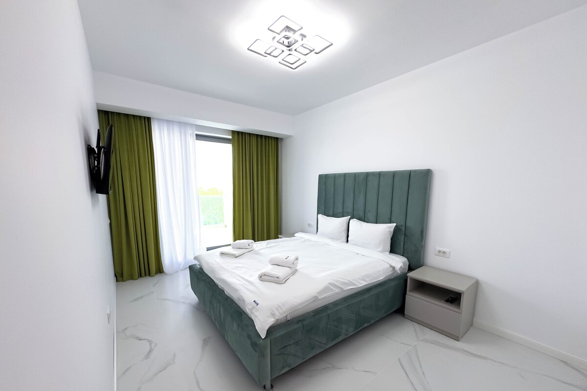 Habitación de hotel moderna con una cama grande, una mesita de noche y vistas al exterior.