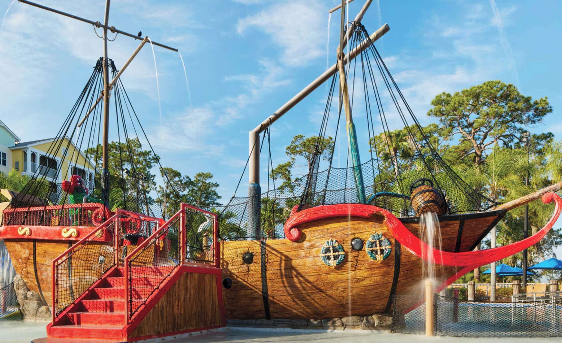 A pirate-themed play area with a ship structure, a red staircase, and a rope bridge.