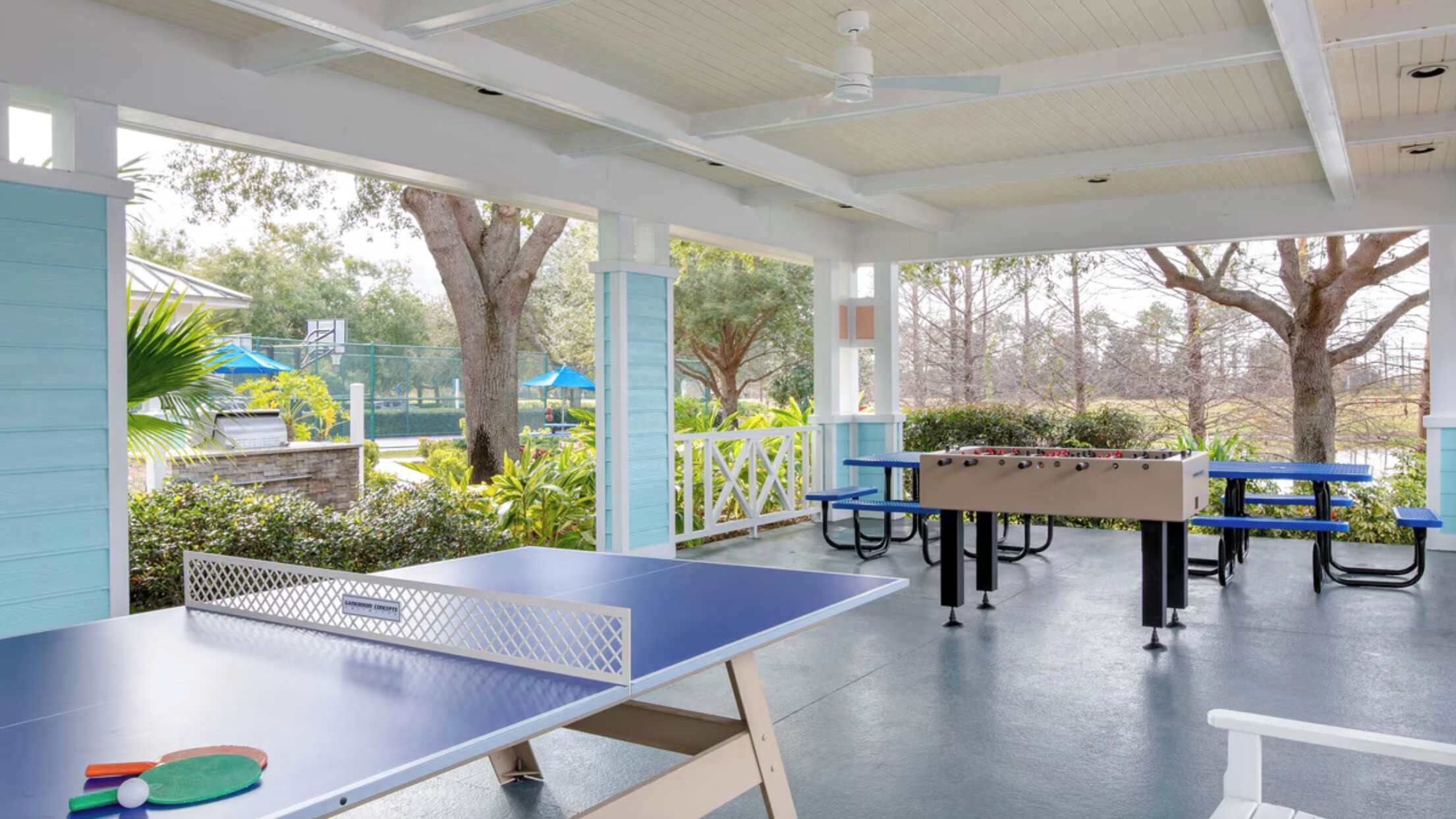 Un espacio recreativo al aire libre con mesa de ping pong, mesa de fútbol de mesa y mesas de picnic.