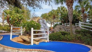 Un parcours de mini-golf doté d’une surface de jeu bleue, de bordures blanches et d’une cascade.