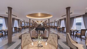 Un amplio vestíbulo de hotel con un piano de cola, elegantes asientos y un mostrador de recepción de mármol.