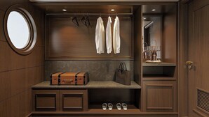 Un vestidor bien iluminado con detalles de madera, un espejo redondo, ropa colgada, una maleta, un bolso de mano y un zapatero.