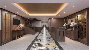 Vestíbulo de hotel con suelo de mármol, una recepción, una escalera y paneles decorativos en la pared.