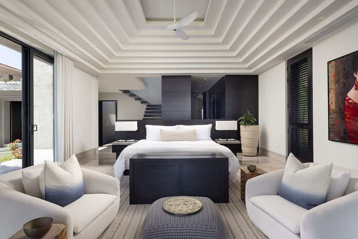 Une chambre moderne avec un grand lit, deux tables de chevet, un ventilateur de plafond et une grande fenêtre.