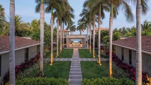 Un resort con un sendero central que conduce a una zona de piscina, rodeado de palmeras y céspedes cuidados.