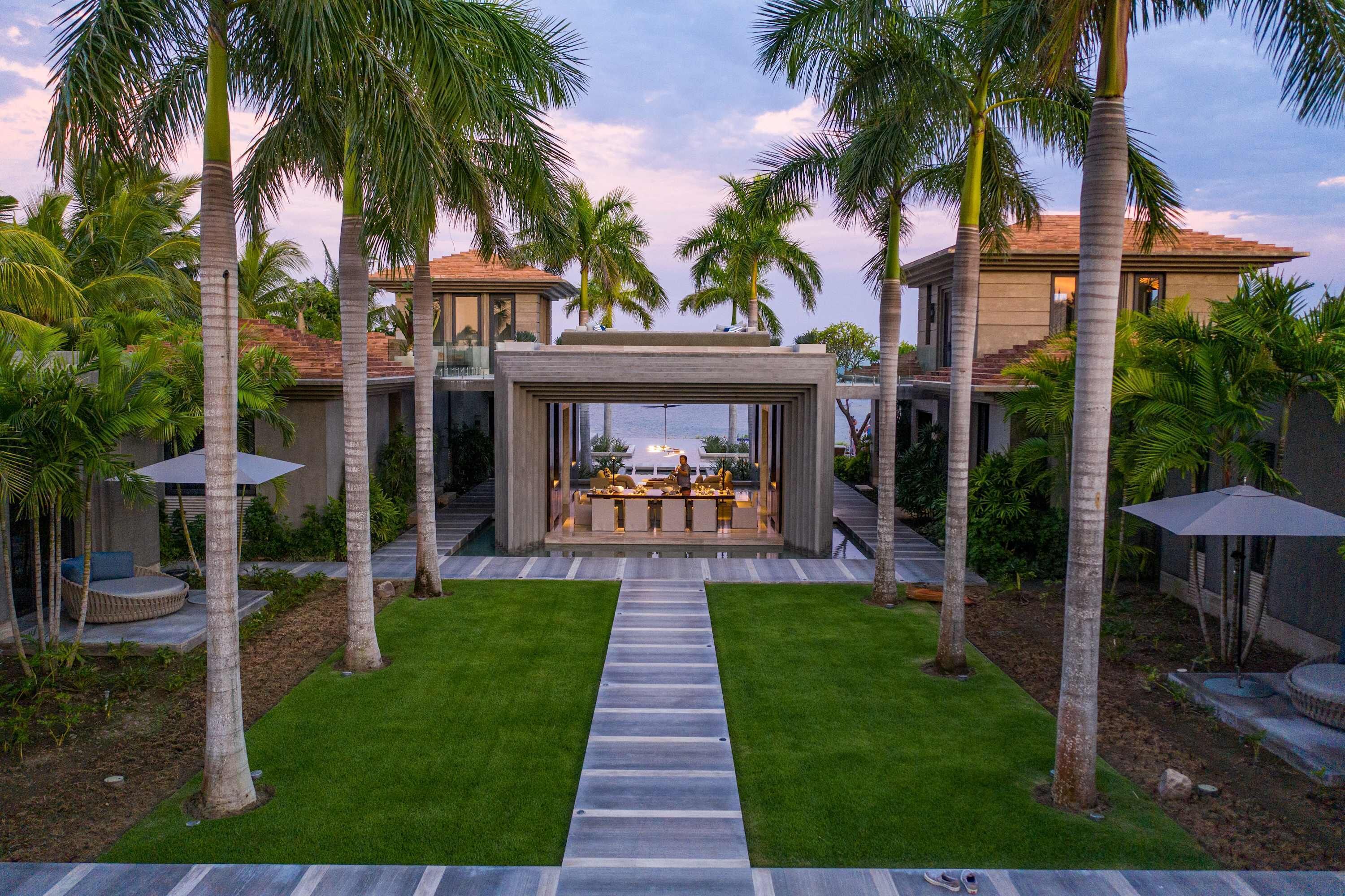 Una casa moderna con un patio central, rodeada de palmeras y vistas al océano.