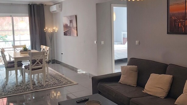 A modern living room with a sofa, a dining table with chairs, a rug, and a large window with curtains. - Spacious Family Apartment in Málaga, near historic center (Málaga)