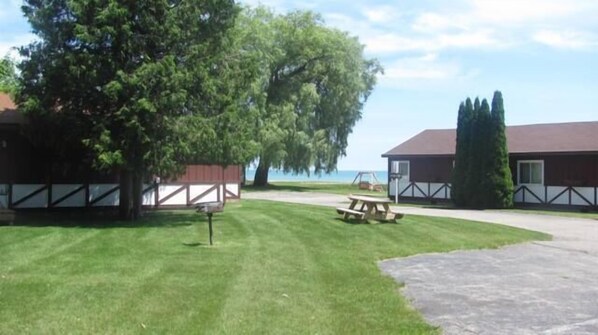 A grassy area with a picnic table and a basketball hoop. There are two buildings with a fence in the background.