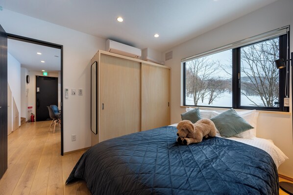 A bedroom with a large bed, a window with a view of trees, a wardrobe, and a chair. - Niseko Town, Toyosato B near Hirafu, Niseko village and 30' Risutsu (NISEKO)
