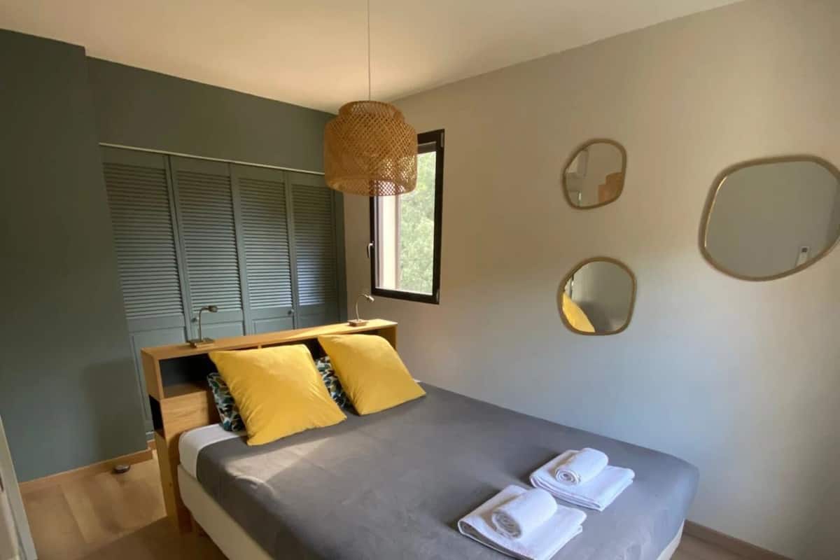 A bedroom with a bed, a window, and a mirror on the wall.