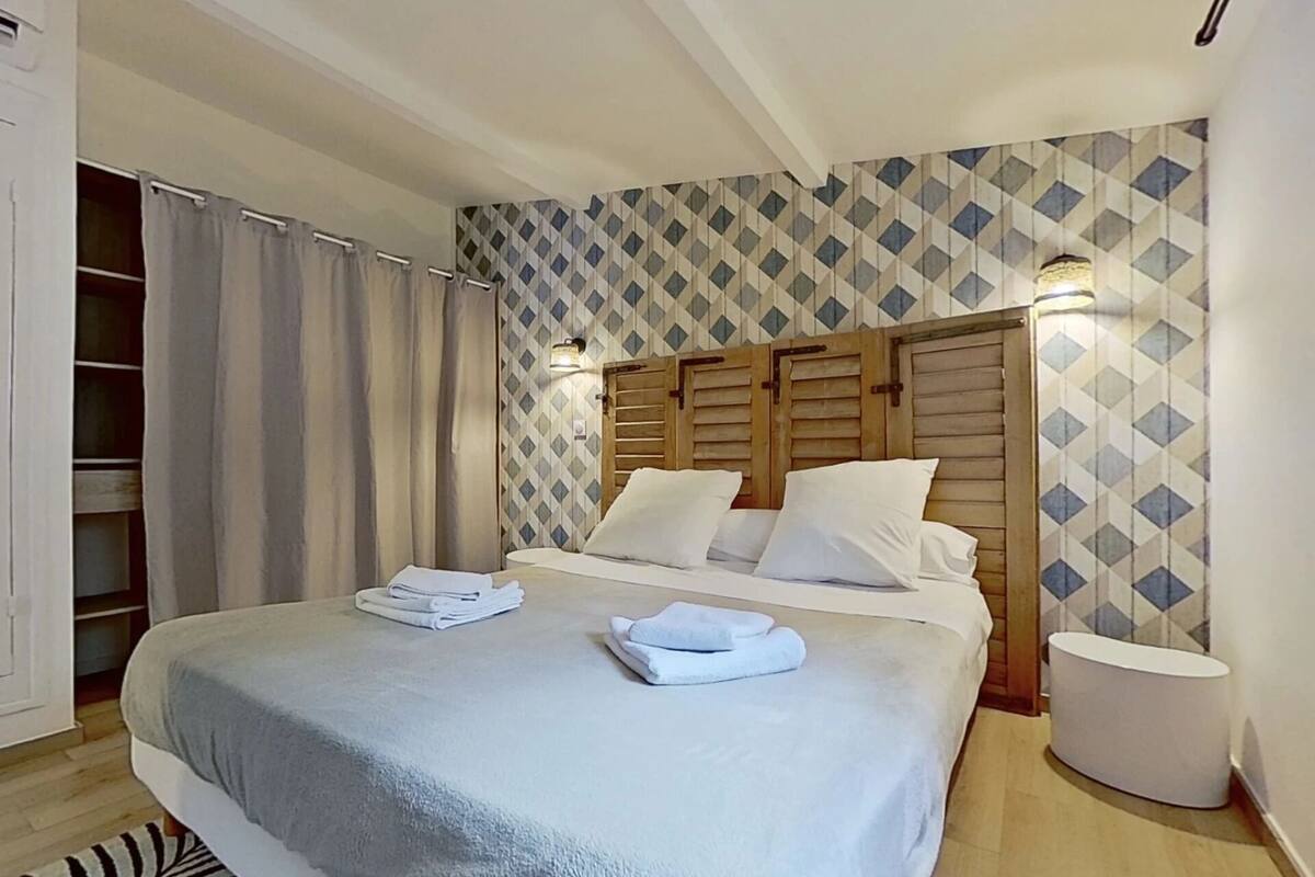 A neatly made bed with white linens, a wooden headboard, and a patterned wall.