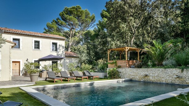 Ein Swimmingpool mit Liegestühlen, einer Pergola und einer Steinmauer.