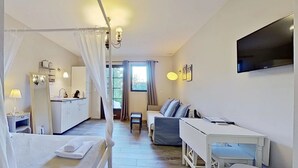 Ein Schlafzimmer mit Baldachinbett, einer kleinen Küchenzeile, einem Essbereich und einem an der Wand montierten Fernseher.