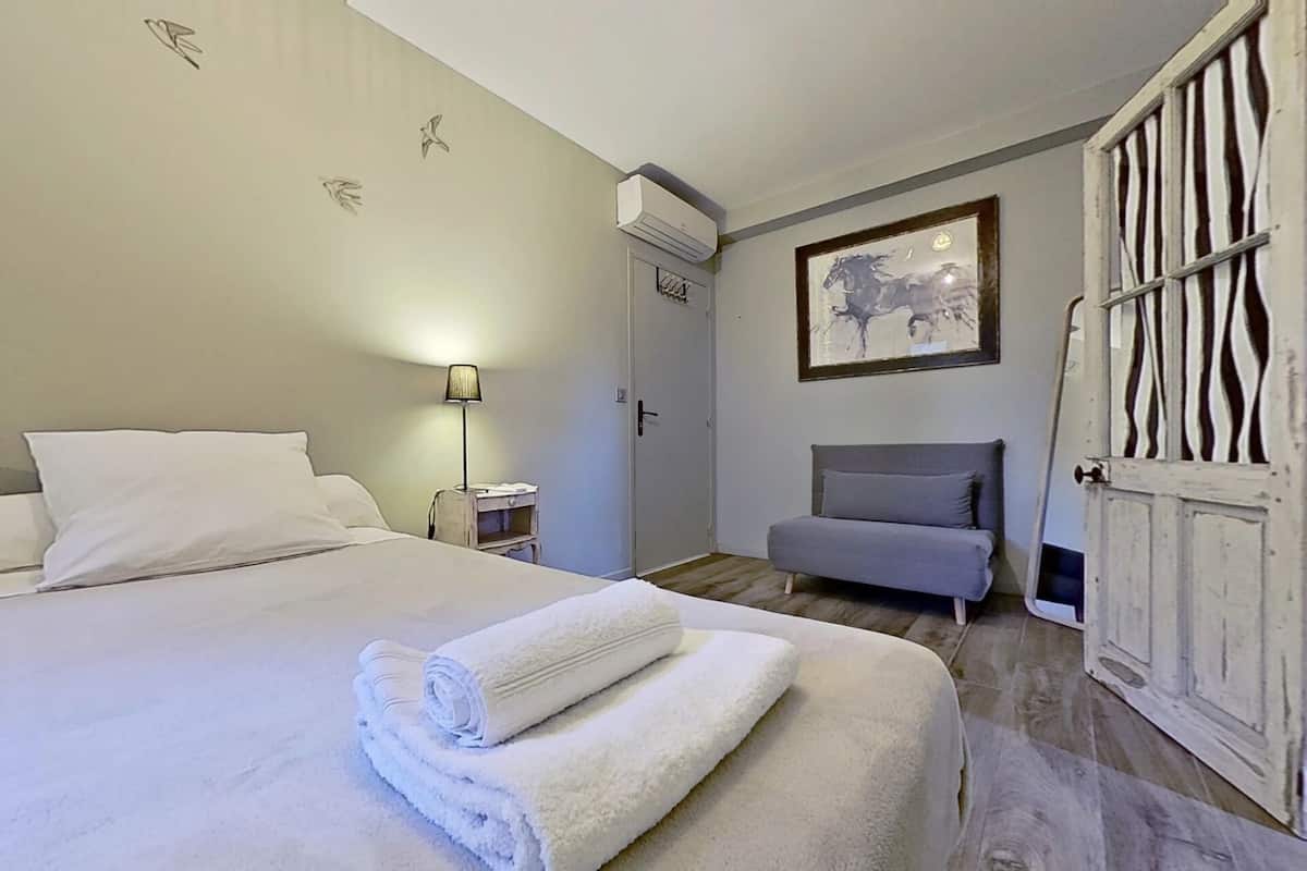 A bedroom with a bed, a nightstand, a lamp, a gray sofa, and a door with a striped pattern.