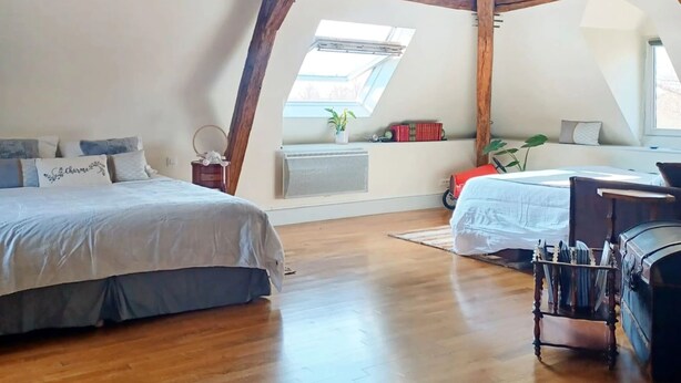 A bedroom with a sloped ceiling, wooden beams, a skylight, a bed, a desk, and a chest of drawers. - Chambres d'hôtes Au Bord De Loire (La Marche)