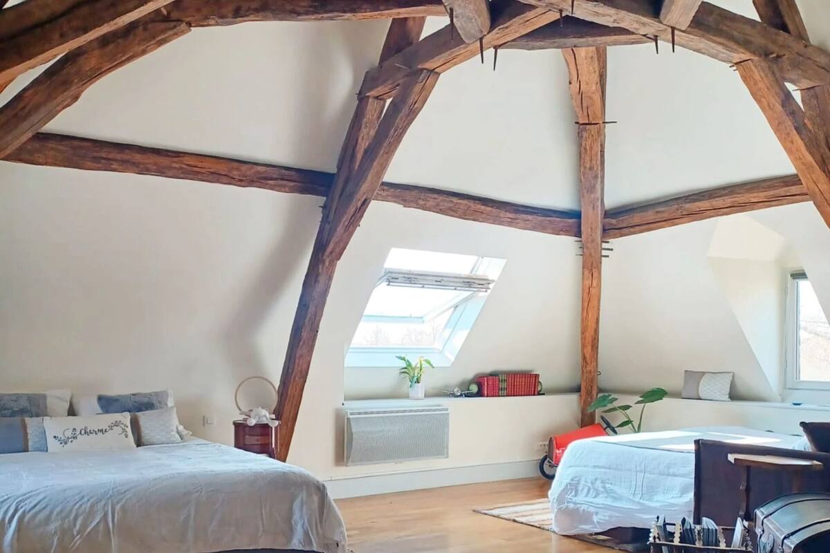 Ein Schlafzimmer mit geneigter Decke, Holzbalken, einem Oberlicht, einem Bett, einem Schreibtisch und einer Kommode.