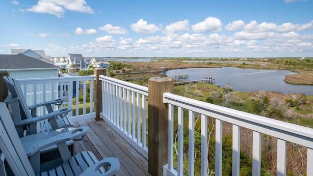 A deck with Adirondack chairs overlooking a lake and houses in the distance. - Still Waters - Waterfront - NEW Design Build Home - Ocean View (North Topsail Beach)
