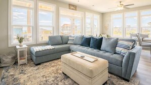A living room with a sectional sofa, ottoman, and a small side table. - Still Waters - Waterfront - NEW Design Build Home - Ocean View (North Topsail Beach)