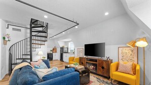 A modern loft apartment with a staircase, living room, kitchen, and a large TV.