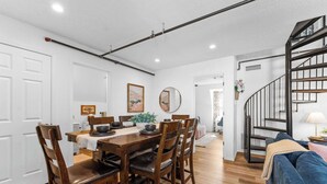 A dining area with a wooden table and chairs, a staircase, and a blue couch.