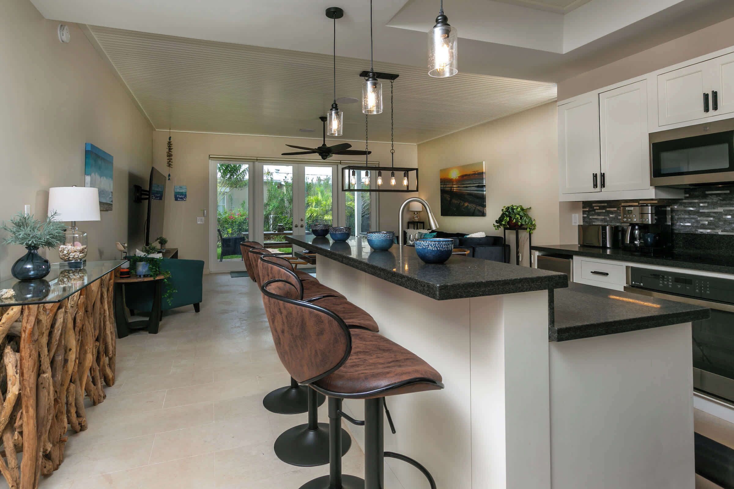 A modern kitchen with a central island, bar stools, and a ceiling fan.
