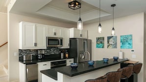 A modern kitchen with white cabinets, stainless steel appliances, a black countertop, and a bar area with stools. - Serenity Villa- Steps from Beach, Family Friendly (Cruz Bay)