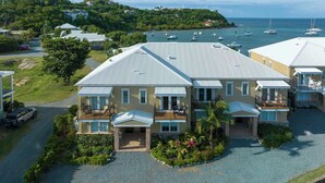 A two-story house with a balcony, a driveway, and a view of the sea with boats. - Nautilus- Beach Front with 3 King Suites (Cruz Bay)