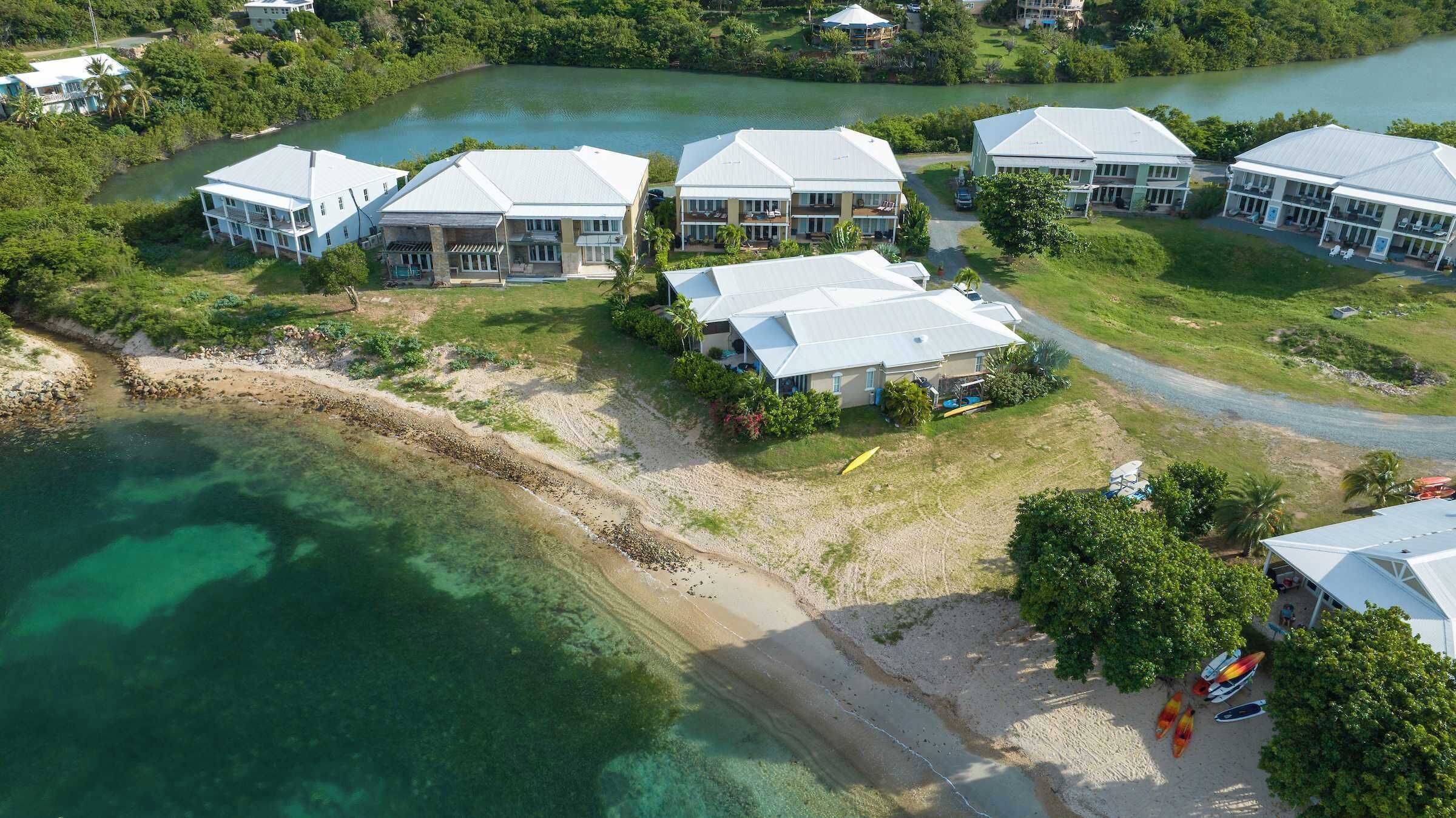Luchtbeeld van een kustresort met meerdere gebouwen, een strand en helder turquoise water.
