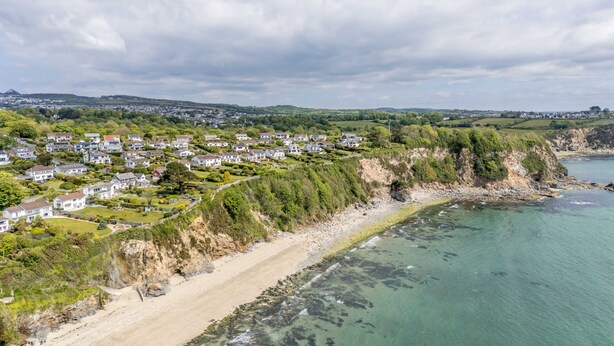 Ett bostadsområde vid kusten med hus som ligger längs en sandstrand och med klippor som reser sig ovanför havet.