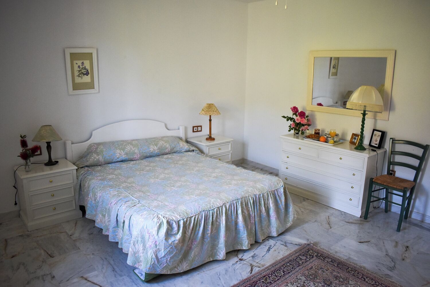Une chambre à coucher comprenant un lit, des tables de chevet, une commode, une chaise, un miroir et un tapis.