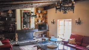 Una sala rústica con chimenea de piedra, una mesa de centro de vidrio y un sofá de cuero rojo.