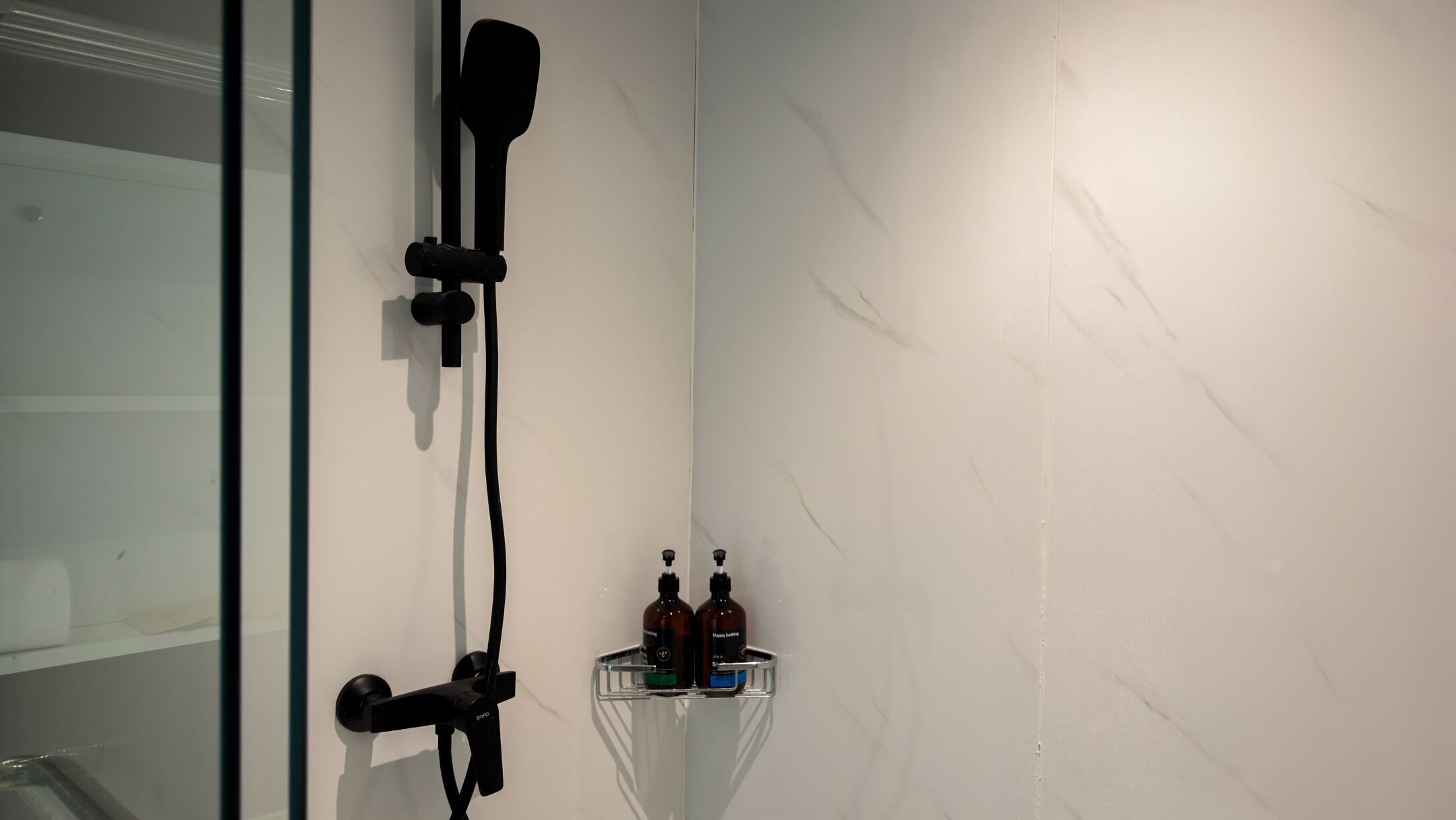 A bathroom with a glass shower enclosure, a faucet, and a shelf with two bottles.