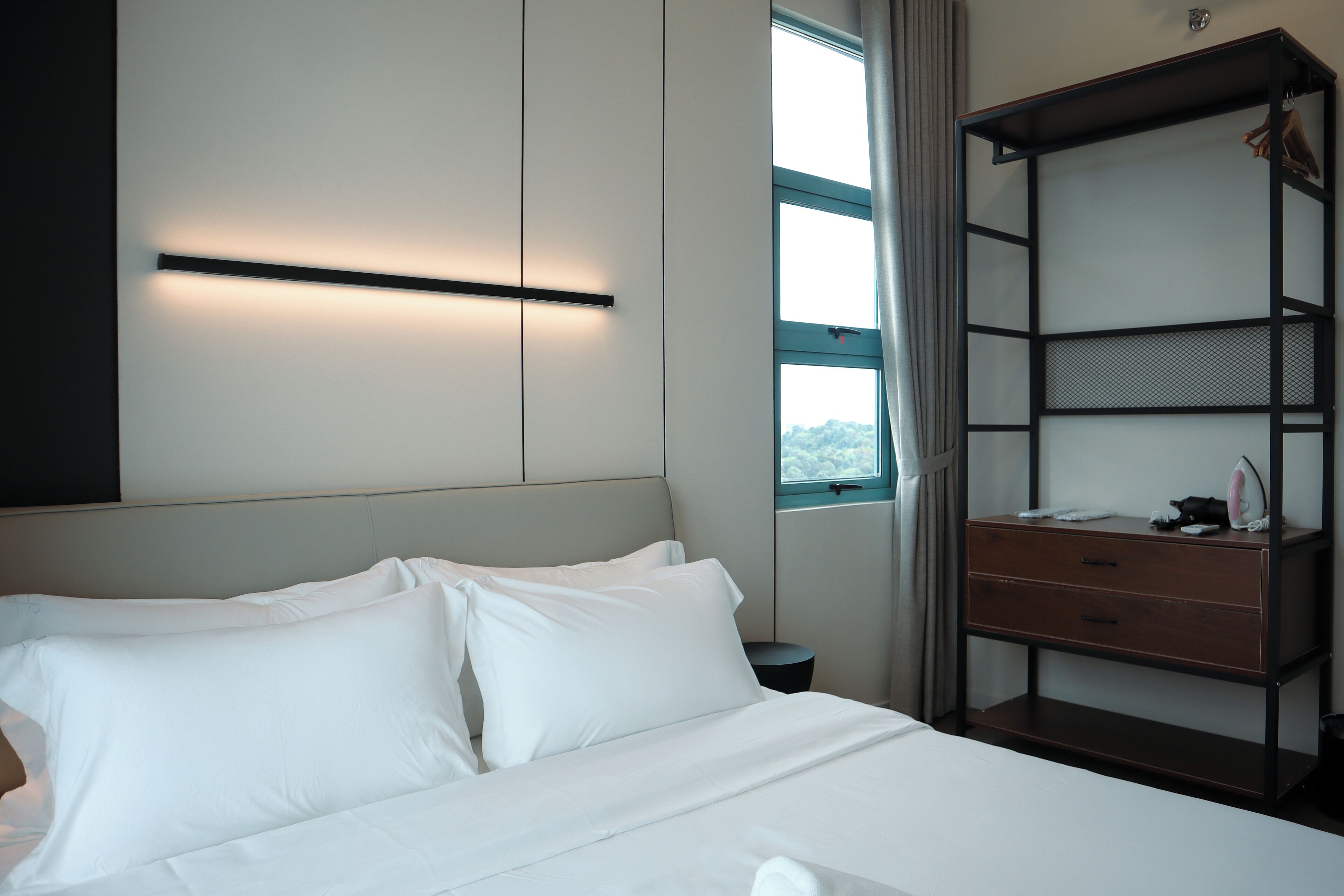Una habitación de hotel con cama, mesita de noche, armario y ventana con cortinas.
