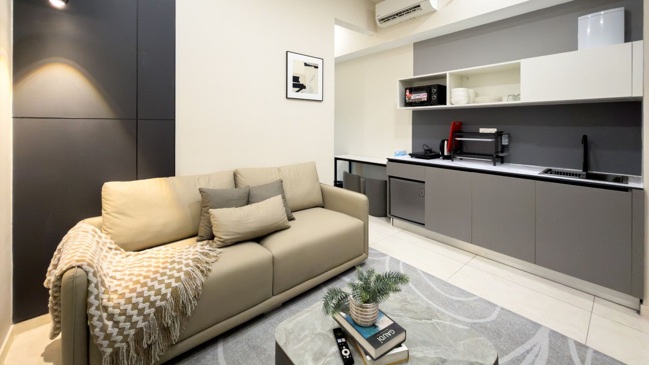 Een moderne woonkamer met een bank, een salontafel en een keukenhoek met een magnetron, koffiezetapparaat en kastjes.
