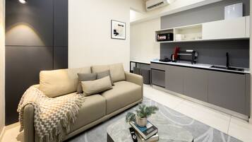 Een moderne woonkamer met een bank, een salontafel en een keukenhoek met een magnetron, koffiezetapparaat en kastjes.