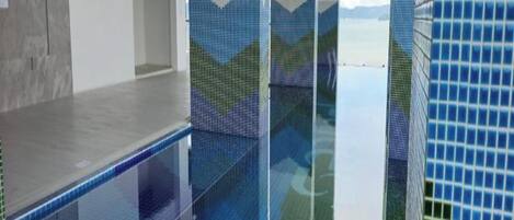 An indoor swimming pool with clear glass walls, a tiled floor, and a metal ladder.