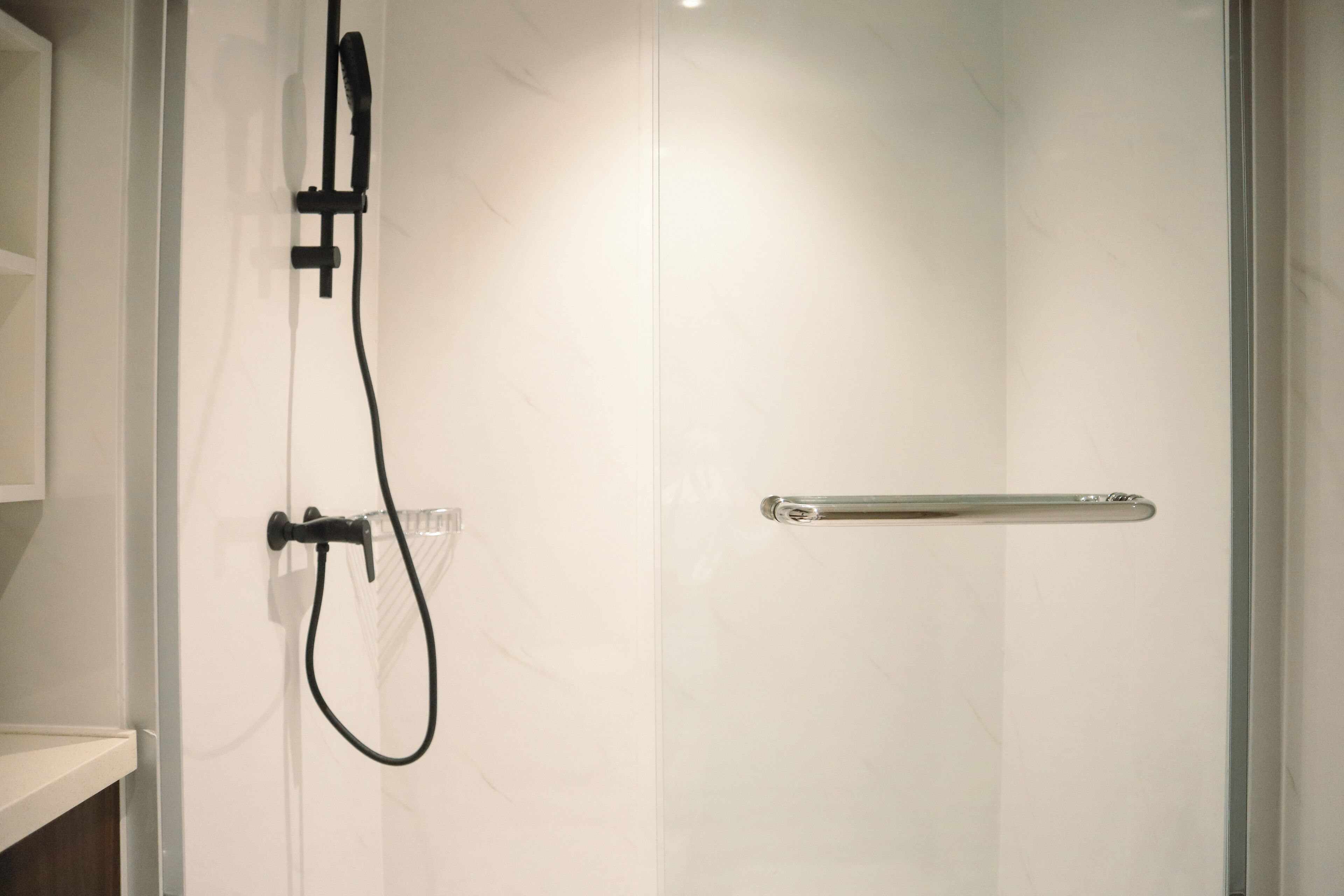 A glass-enclosed shower with a handheld showerhead and a handheld shower attachment.