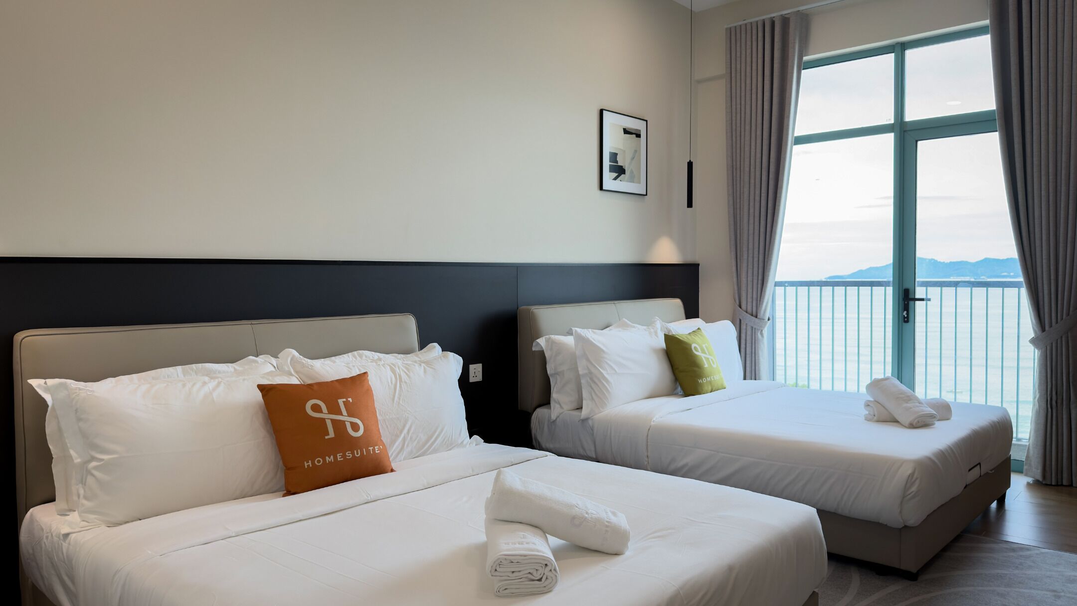 Une chambre d’hôtel avec deux lits, une grande fenêtre donnant sur un beau paysage et un tableau encadré au mur.