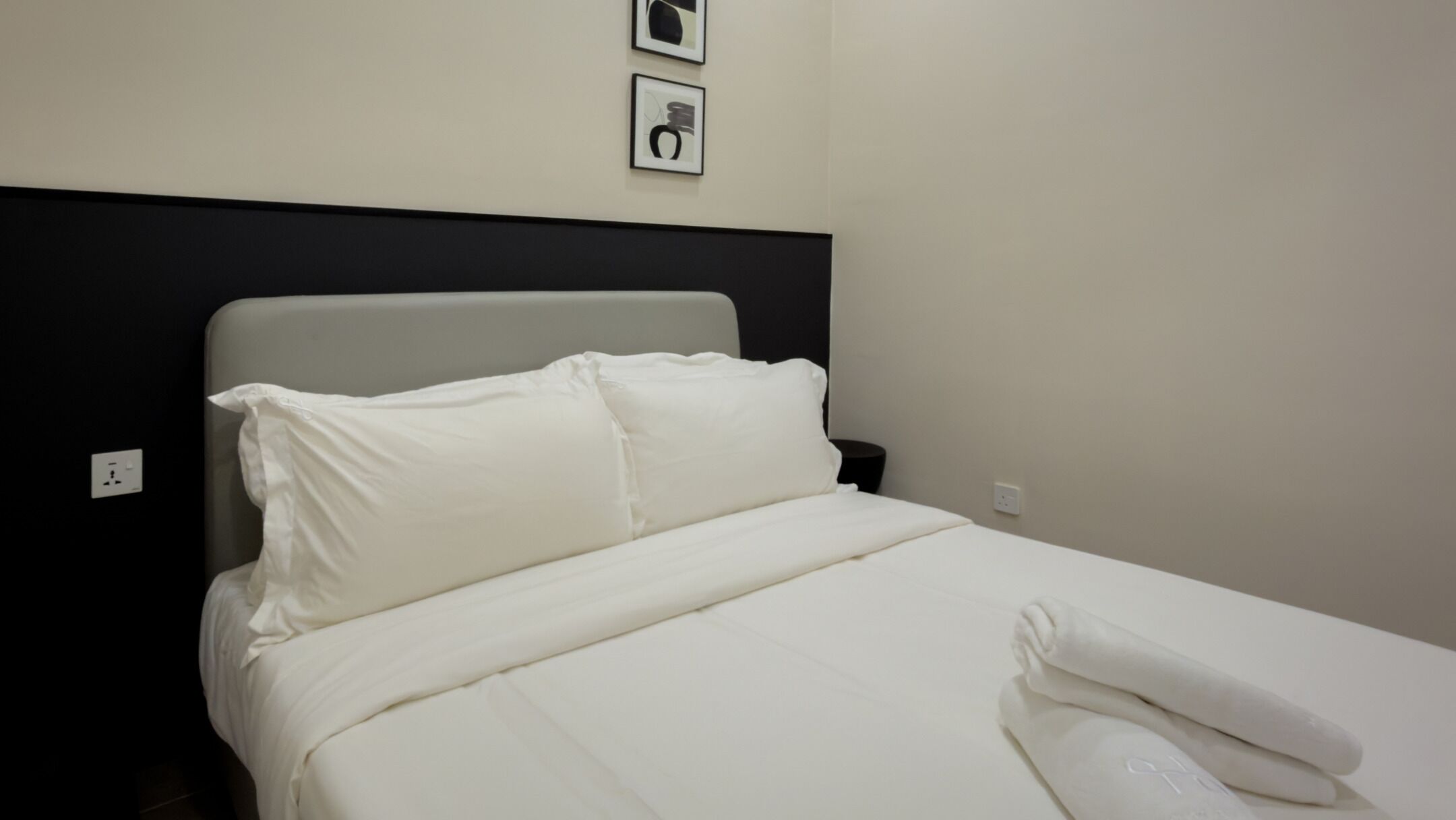 A neatly made bed with white bedding and pillows, a black headboard, and a small nightstand with a lamp.