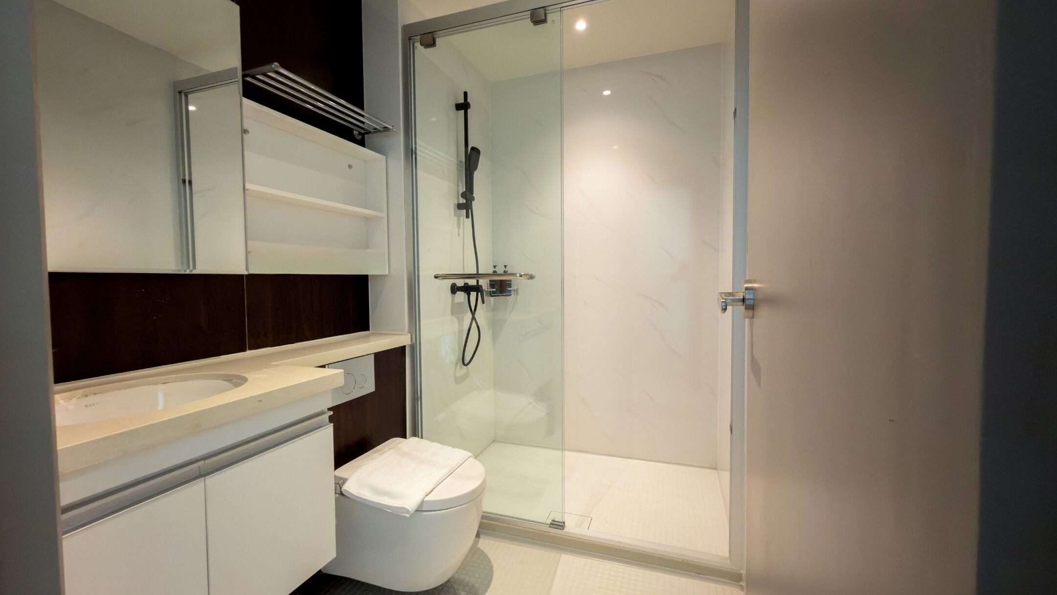 A modern bathroom with a glass shower enclosure, a white toilet, and a vanity with a mirror and shelves.