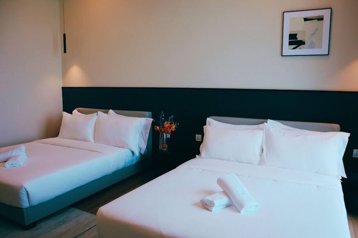 A hotel room with two beds, a nightstand with a vase of flowers, and a framed picture on the wall.
