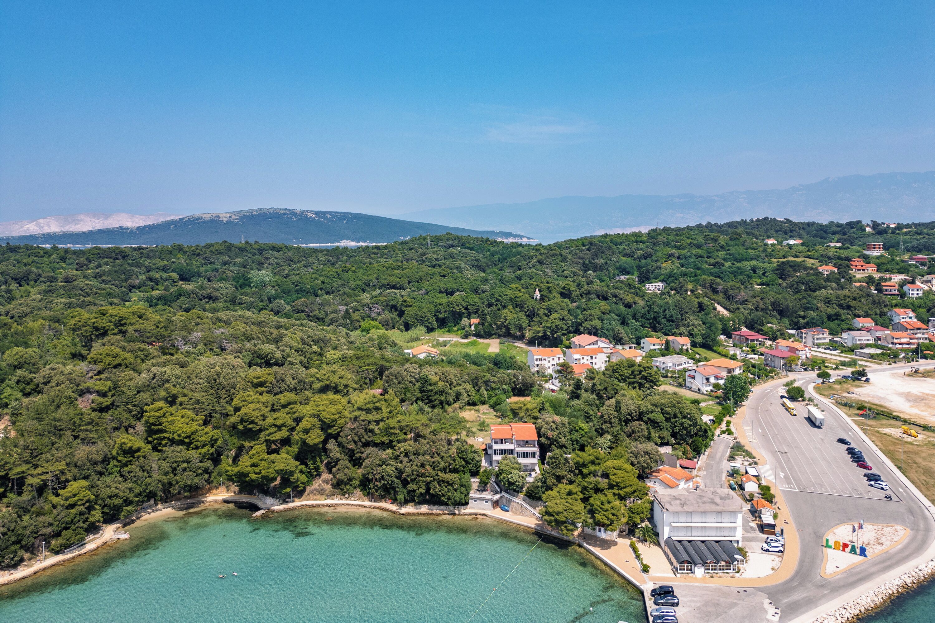An aerial view of a coastal town with a clear road, buildings, and a beach.
