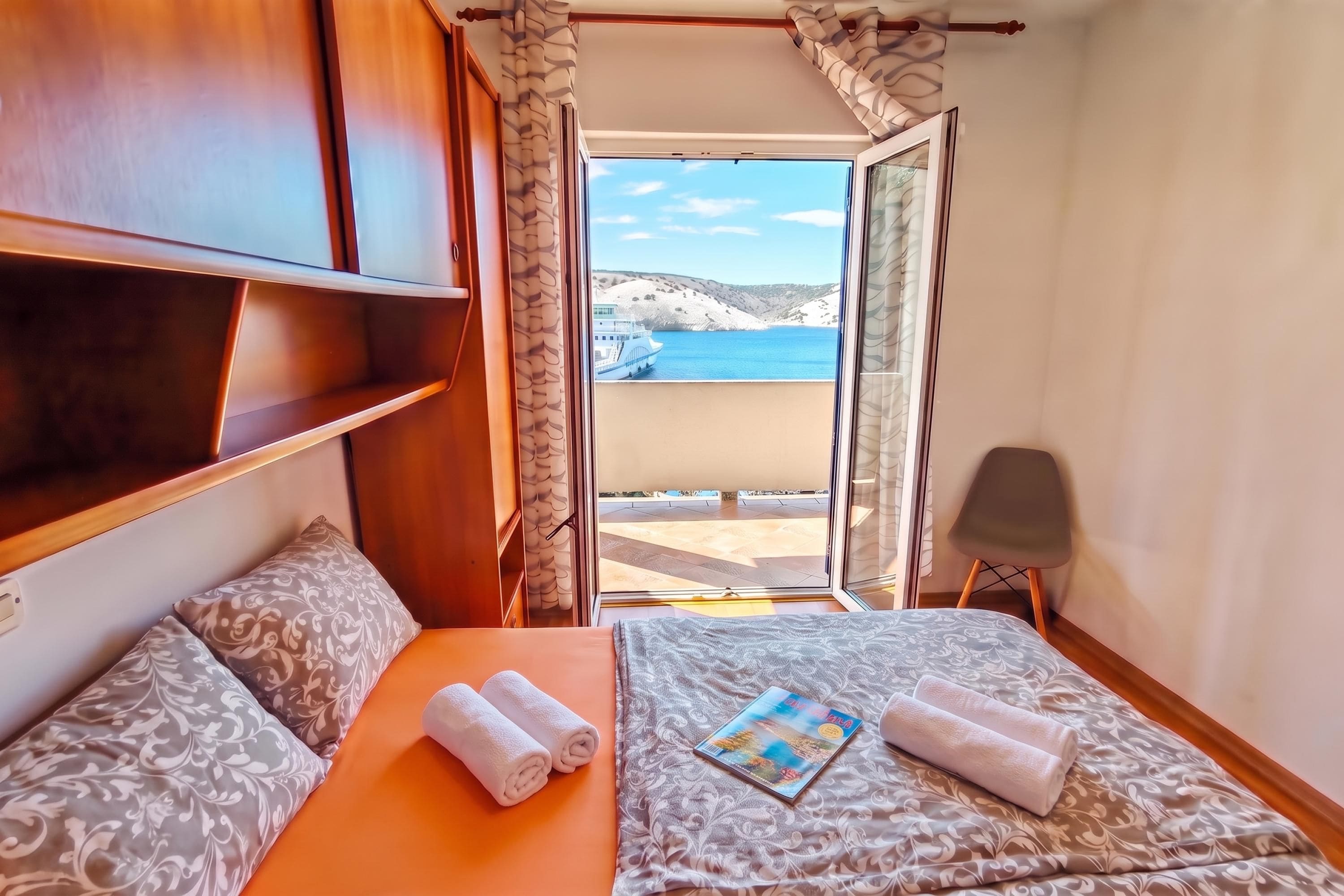 Una stanza con un letto, due cuscini, una rivista e asciugamani.