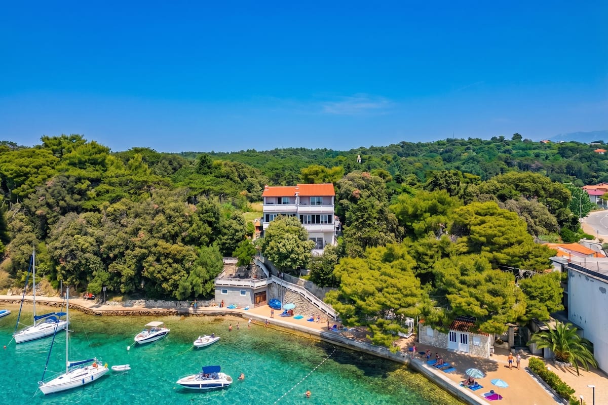 Una propiedad costera con un edificio grande, un muelle con barcos y una zona de playa.